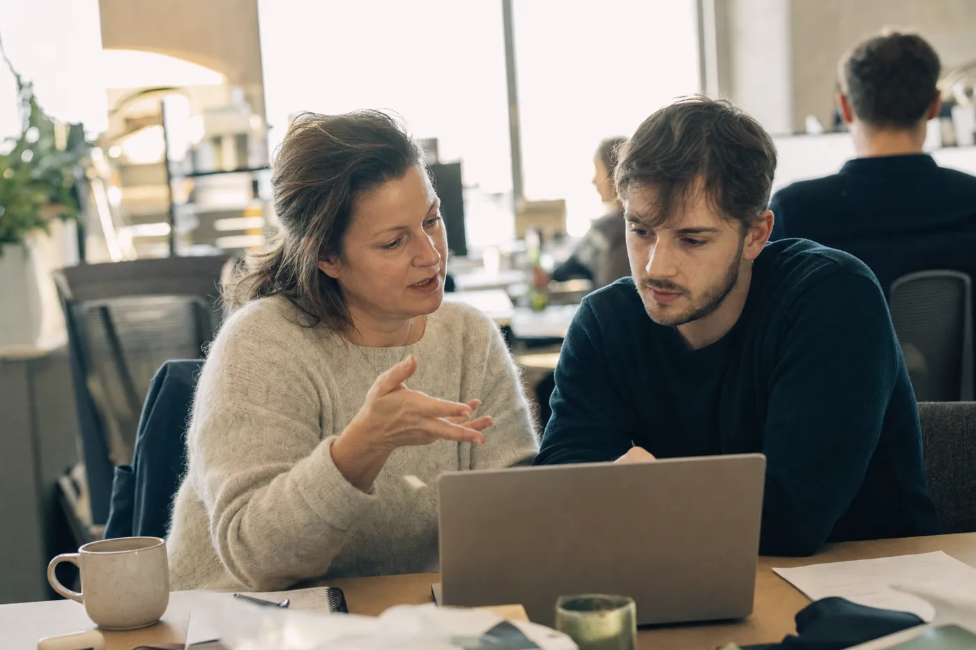 A manager coaching a team member through AI training for managers at a shared desk in warm morning light