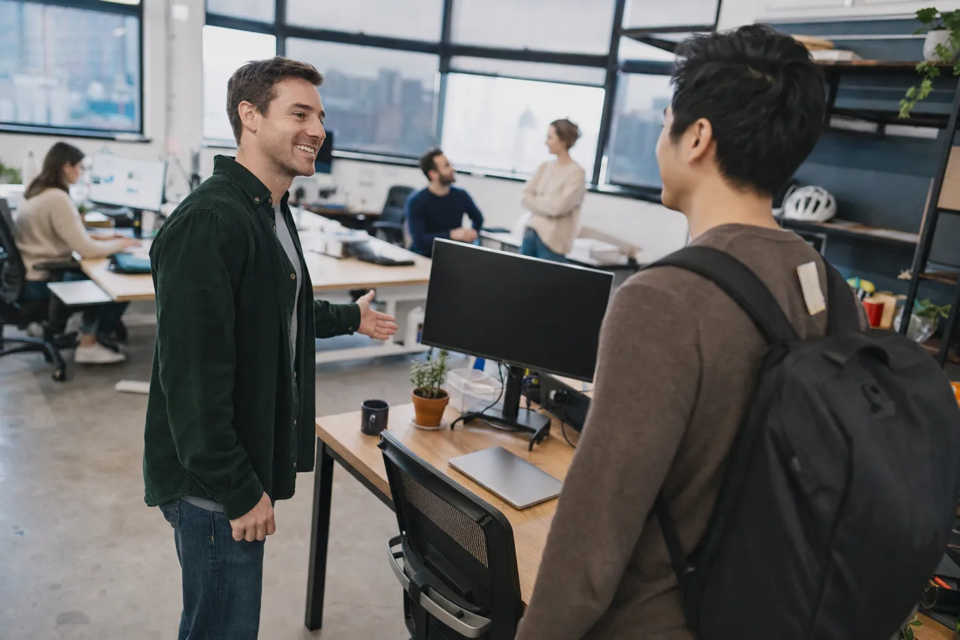 A new hire being welcomed to his desk by a teammate on his first morning, following employee onboarding best practices