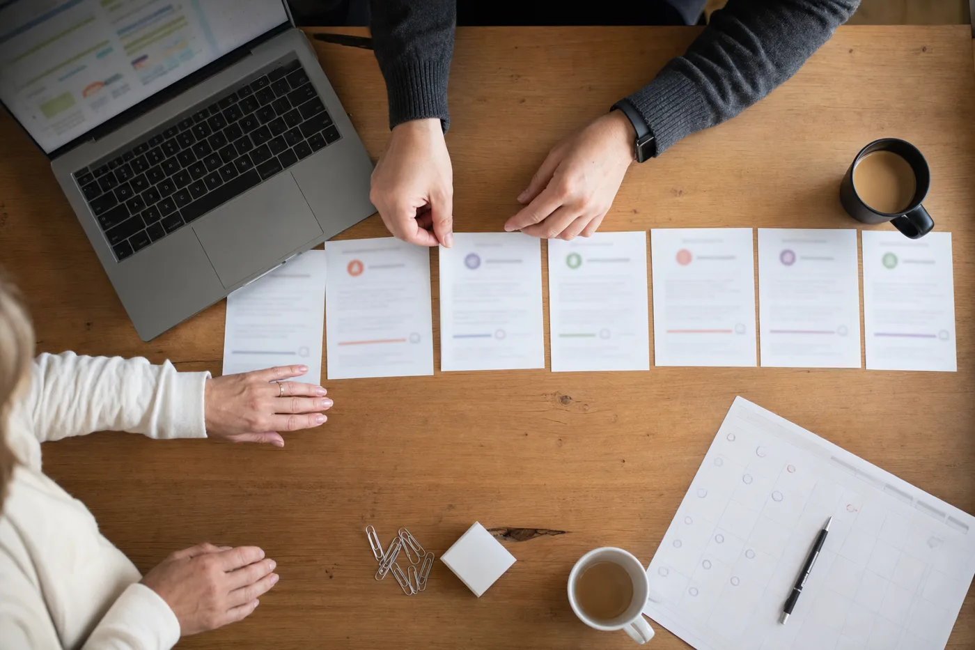 Hands laying out a row of schedule cards on a desk, planning an employee onboarding timeline from first day to ninety days