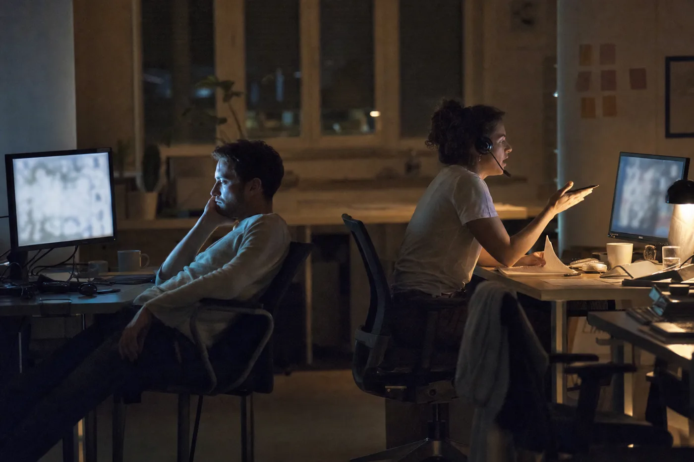 Two desks at evening, one passive viewer lit by a flat blue screen beside an engaged learner in a live interactive session