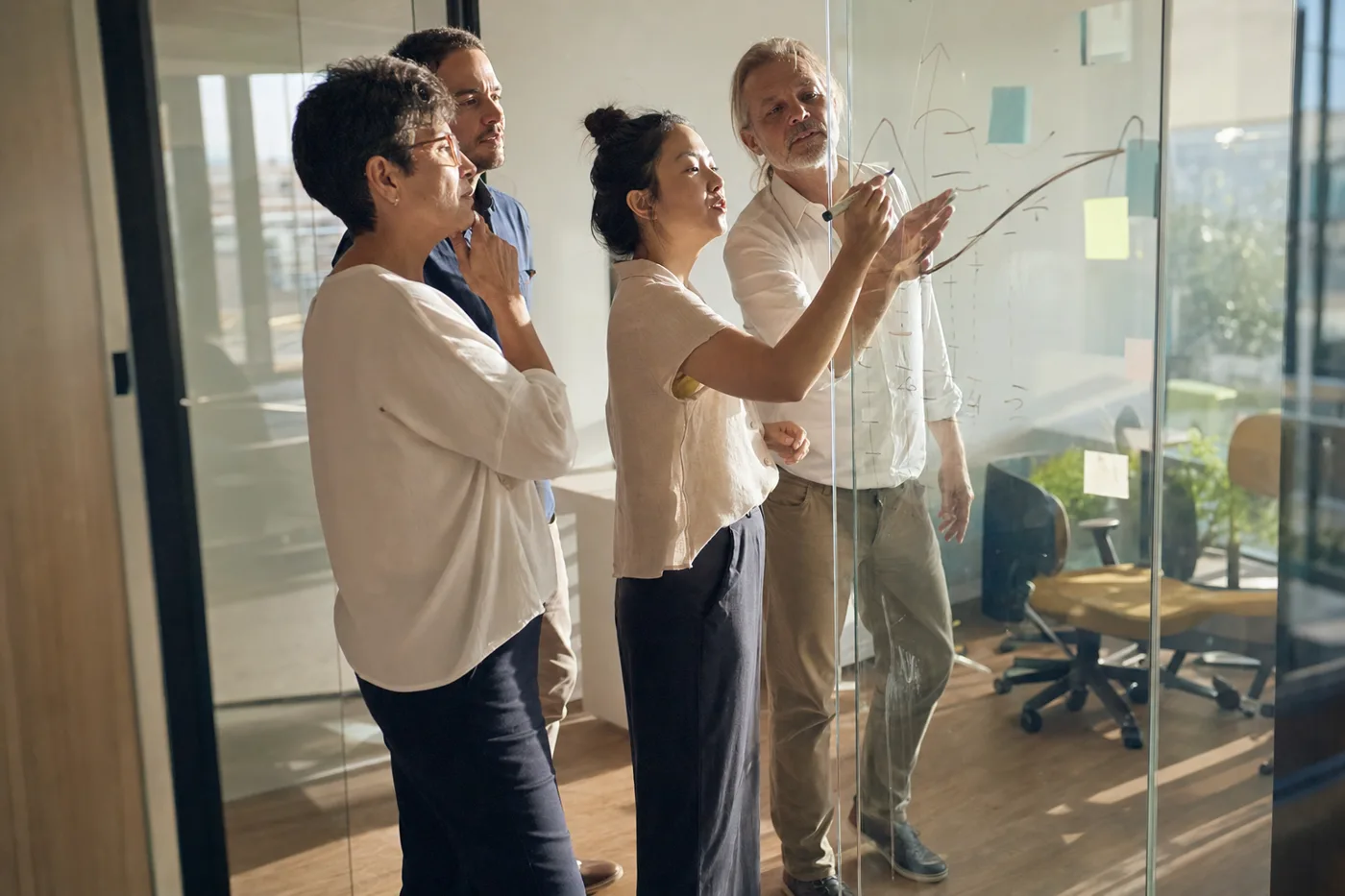 Four colleagues at a glass wall sketching a rising curve, working through a training design problem together