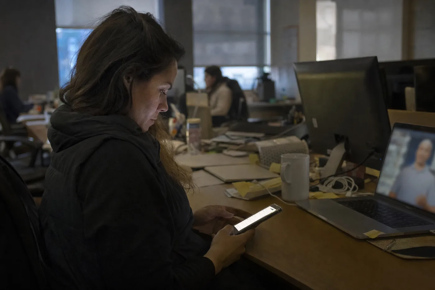 An employee multitasking during training, checking her phone while a training video plays unattended on her laptop